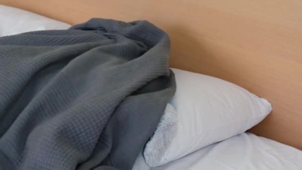 Грустный мальчик лежит на кровати с лихорадкой и головной болью и у него болит голова. Покрытый одеялом на голове. Он смотрит из-под одеяла и недовольно бросает мягкую игрушку в — стоковое видео