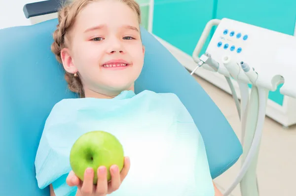 Mädchen im Zahnarztstuhl zeigt grünen Apfel — Stockfoto