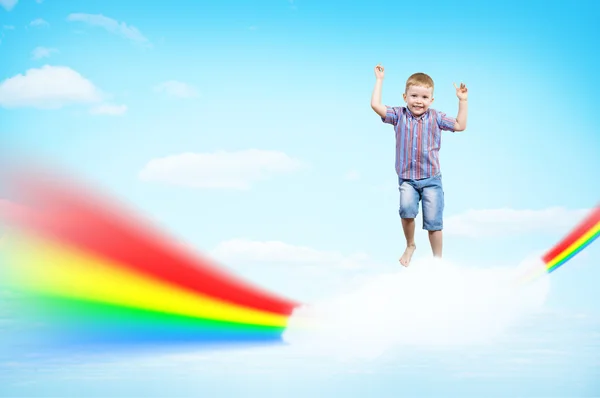 Niño saltando sobre las nubes y un arco iris — Foto de Stock