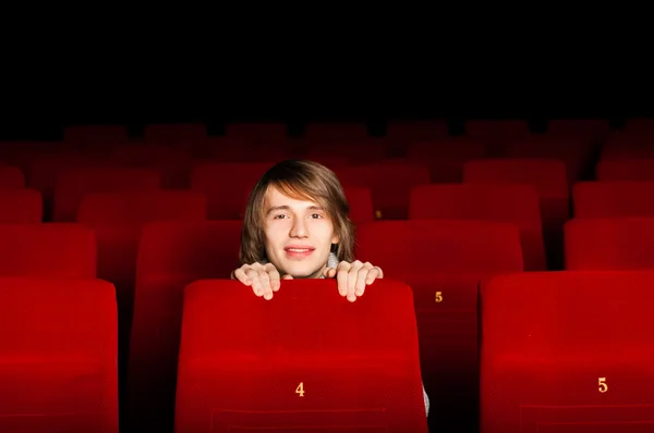 Молодой человек в кинотеатре прячется за стулом — стоковое фото