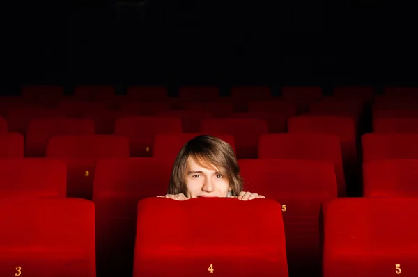 Jovem no cinema escondido atrás de uma cadeira — Fotografia de Stock