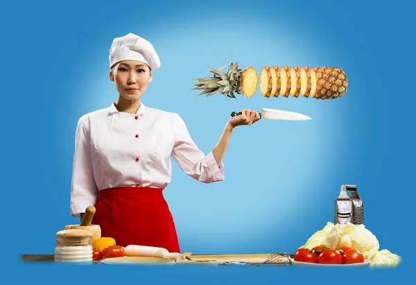 Aziatische vrouwelijke chef-kok snijdt ananas — Stockfoto