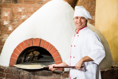 Şef, pizza fırını hamur koyar.,