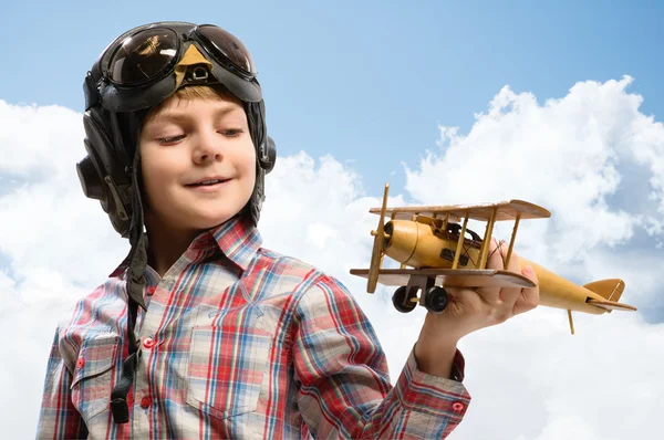 Ragazzo in casco pilota che gioca con un aeroplano giocattolo — Foto Stock