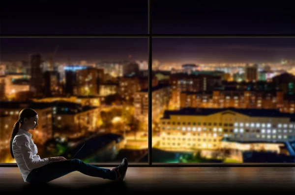 Mujer joven sentada con un portátil junto a la ventana — Foto de Stock