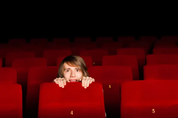 Young man in the cinema hiding behind a chair — Stock Photo, Image