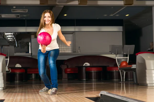 Agradável jovem mulher joga uma bola de boliche — Fotografia de Stock