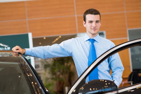 Dealer stands near a new car in the showroom — Stock Photo, Image