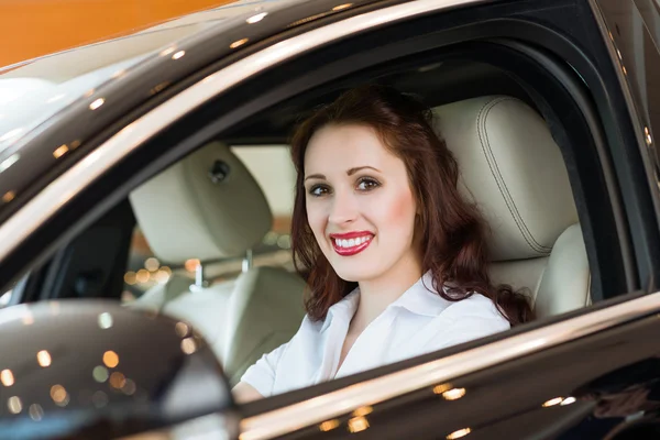 Jovem mulher no carro novo no showroom — Fotografia de Stock