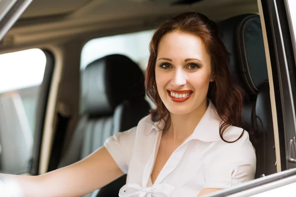 Mujer joven en el coche nuevo en la sala de exposición — Foto de Stock