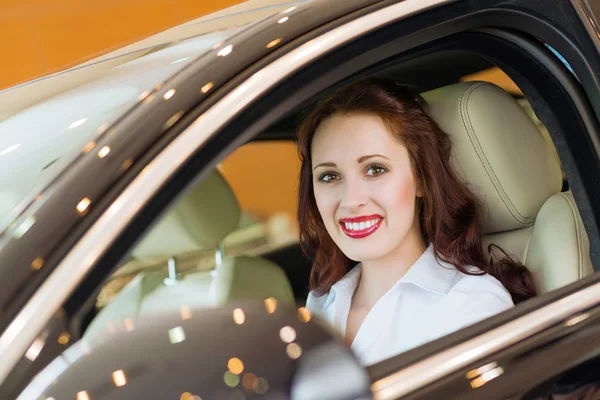 Jovem mulher no carro novo no showroom — Fotografia de Stock