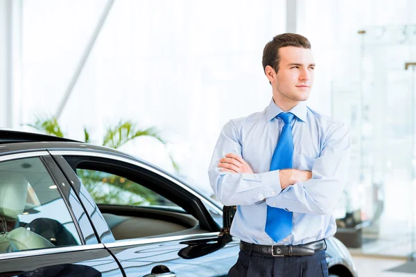 Dealer stands near a new car in the showroom — Stock Photo, Image