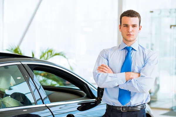 Vendedor fica perto de um carro novo no showroom — Fotografia de Stock