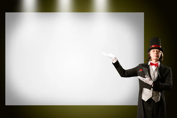 Magician in top hat and tie points to the banner — Stock Photo, Image