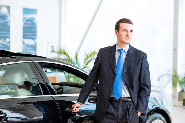 Dealer stands near a new car in the showroom — Stock Photo, Image