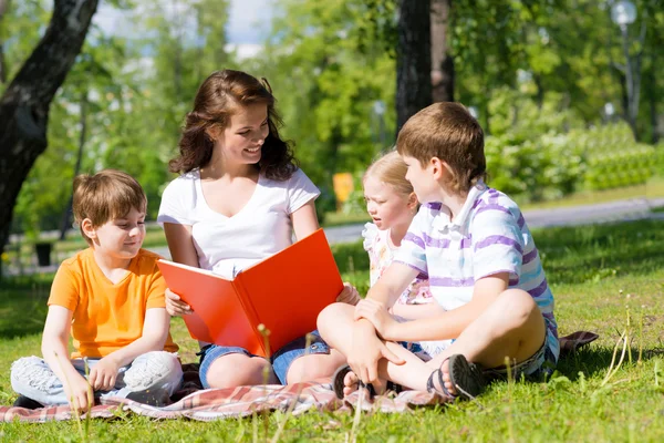 Öğretmen çocuklar için bir yaz parkta bir kitap okur. — Stok fotoğraf