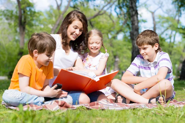 Öğretmen çocuklar için bir yaz parkta bir kitap okur. — Stok fotoğraf