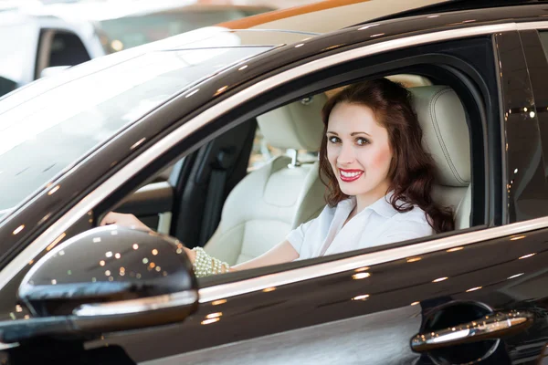 Jovem mulher no carro novo no showroom — Fotografia de Stock