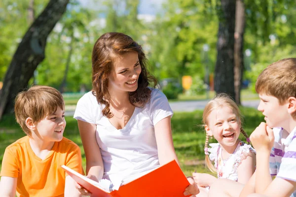 Lehrerin liest Kindern im Sommerpark ein Buch vor — Stockfoto
