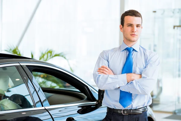 Dealer stands near a new car in the showroom — Stock Photo, Image