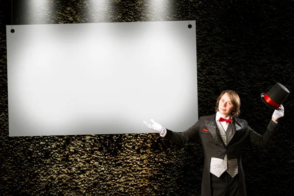 Magician in top hat and tie points to the banner — Stock Photo, Image
