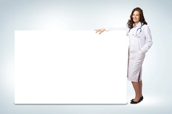Mujer joven médico de pie cerca de una pancarta en blanco — Foto de Stock