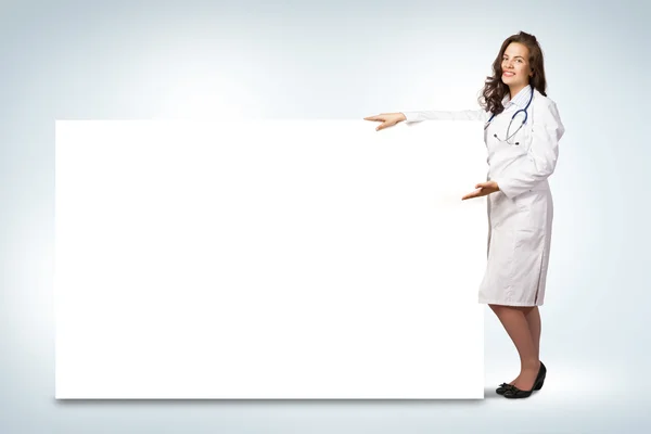 Giovane donna medico in piedi vicino a un banner vuoto — Foto Stock