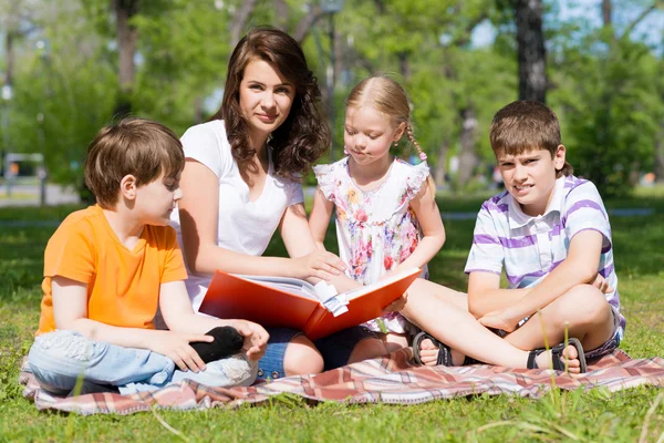 Enseignant lit un livre aux enfants dans un parc d'été — Photo