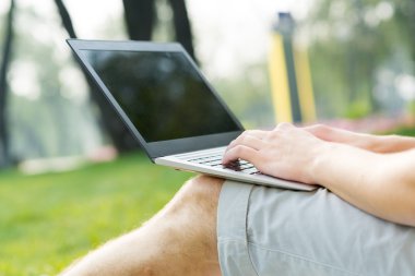 Parkta dizüstü bilgisayarla çalışan genç bir adam.