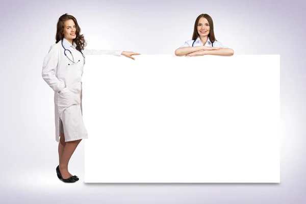 Two young woman doctor holding a blank banner — Stock Photo, Image