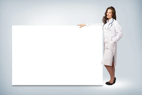 Young woman doctor standing near a blank banner — Stock Photo, Image