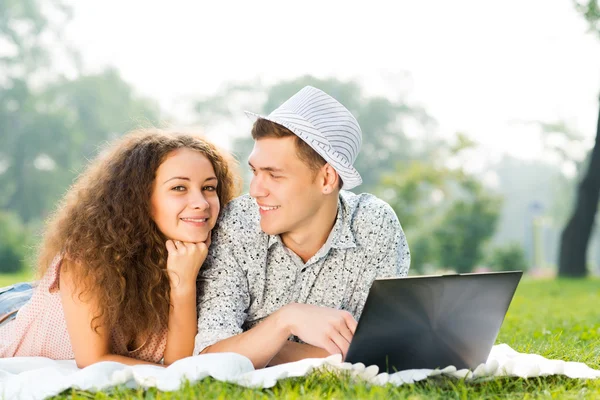 Par liggande tillsammans i en park med laptop — Stockfoto