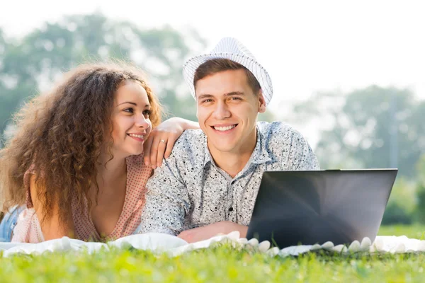 Paar liggen samen in een park met laptop — Stockfoto