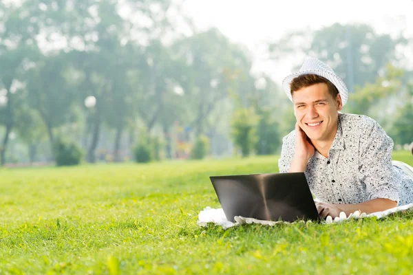 Joven que trabaja en el parque con un ordenador portátil — Foto de Stock