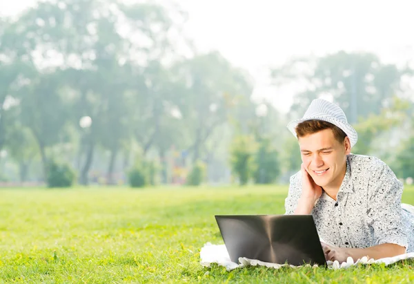Joven que trabaja en el parque con un ordenador portátil — Foto de Stock