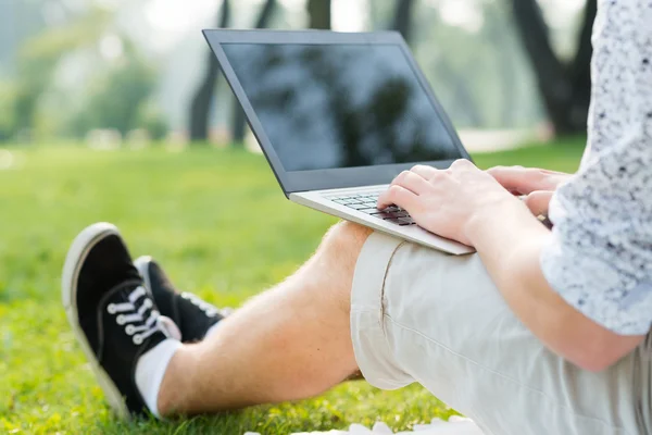 Giovane che lavora nel parco con un computer portatile — Foto Stock