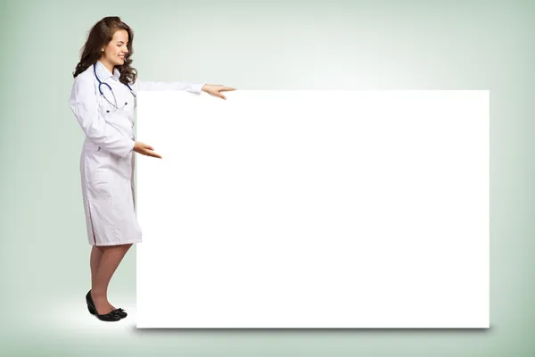 Young woman doctor standing near a blank banner — Stock Photo, Image