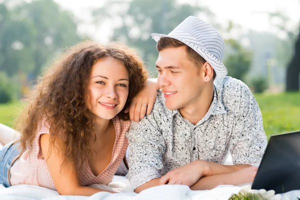 Par liggande tillsammans i en park med laptop — Stockfoto