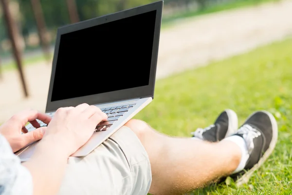 Giovane che lavora nel parco con un computer portatile — Foto Stock