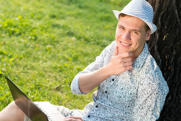 Giovane che lavora nel parco con un computer portatile — Foto Stock