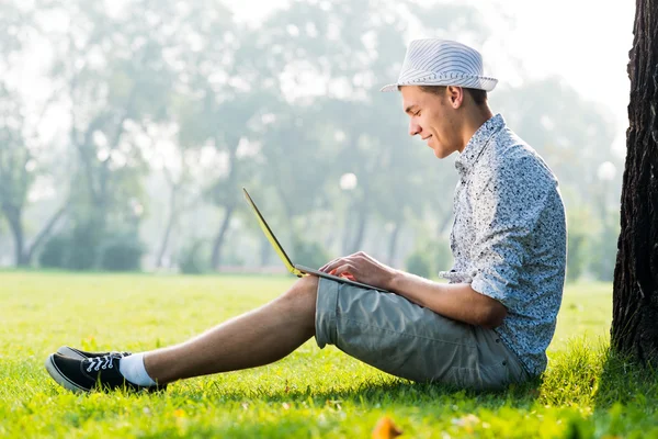 Jeune homme travaillant dans le parc avec un ordinateur portable — Photo