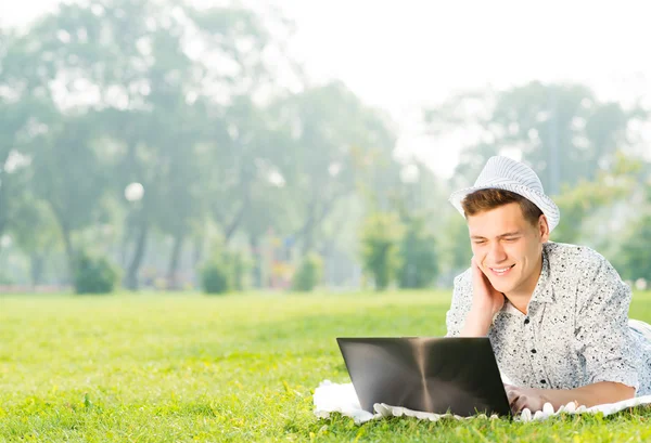 Giovane che lavora nel parco con un computer portatile — Foto Stock