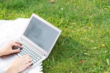 Parkta dizüstü bilgisayarla çalışan genç bir adam.