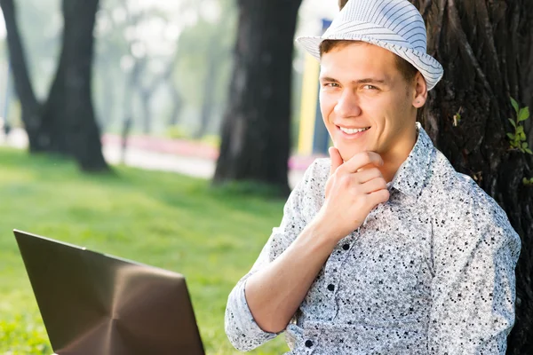 Giovane che lavora nel parco con un computer portatile — Foto Stock