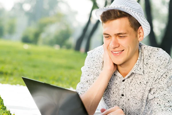公園でノートパソコンを持って働いている若い男が — ストック写真