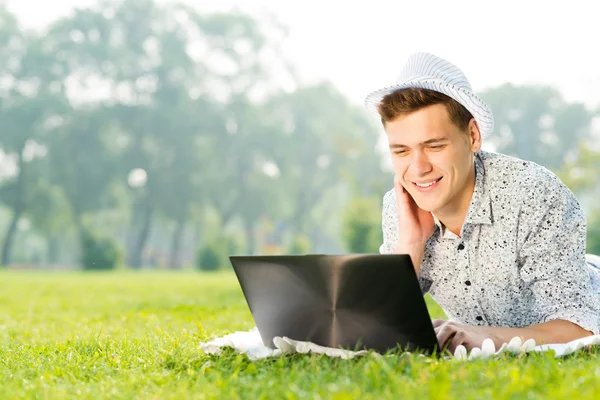 Giovane che lavora nel parco con un computer portatile — Foto Stock