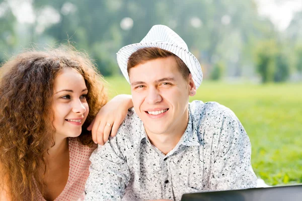Couple lying together in a park with laptop — Stock Photo, Image