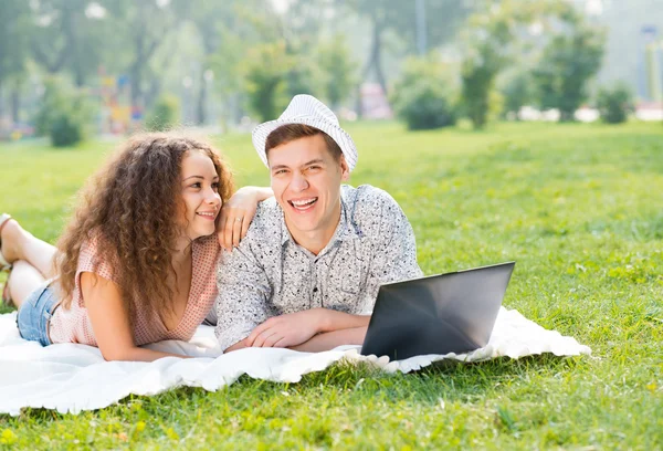 Casal deitado juntos em um parque com laptop — Fotografia de Stock