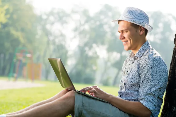 Giovane che lavora nel parco con un computer portatile — Foto Stock