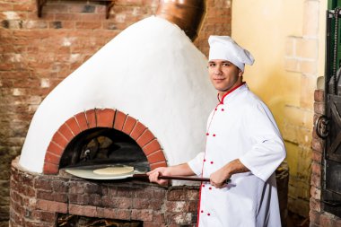 Şef, pizza fırını hamur koyar.